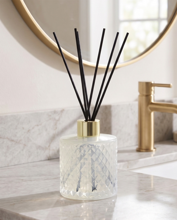 Duftpinde i hvid glasflaske med dekorativt mønster og guldfarvet kant